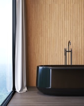 Une salle de bain avec une baignoire noire devant un mur en bardage bois à coté d'une fenêtre