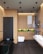 A modern bathroom features minimalistic design elements with wooden panel walls and a sleek black freestanding bathtub. The space includes a white toilet and a contemporary glass shower enclosure. Above the toilet, there is a built-in shelf with green plants providing a touch of nature to the decor. Dual white sinks are installed on a floating counter, and the room is well-lit with recessed ceiling lights.