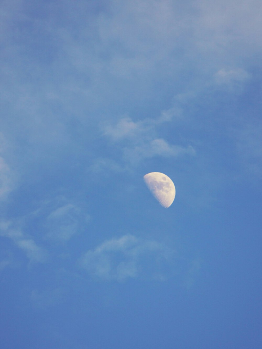 Ein Halbmond am blauen Himmel mit Wolken