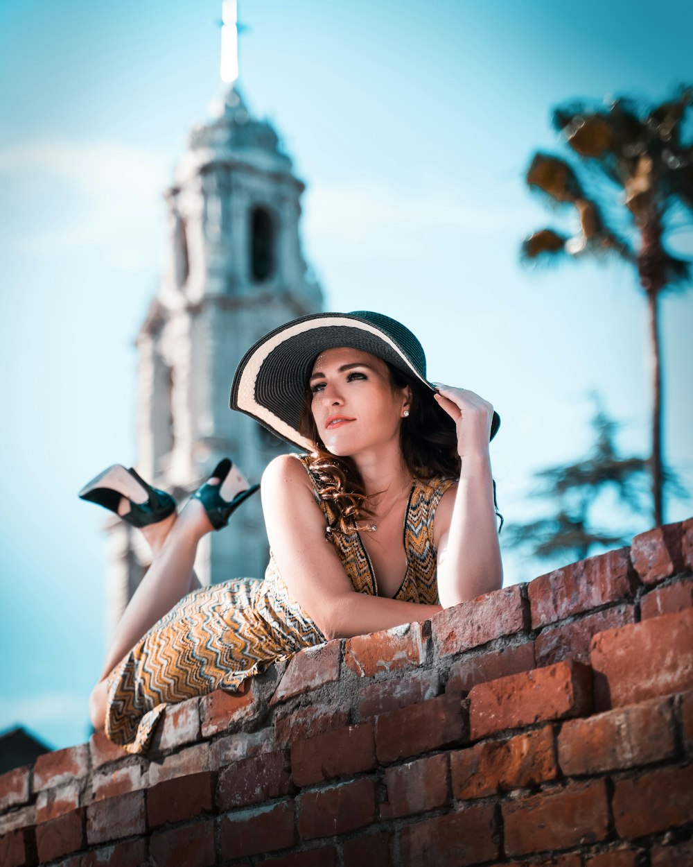 a woman in a hat and dress sitting on a brick wall