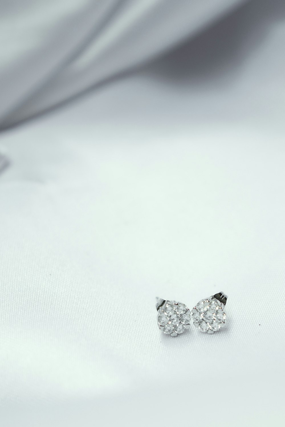 a pair of diamond earrings sitting on top of a white cloth