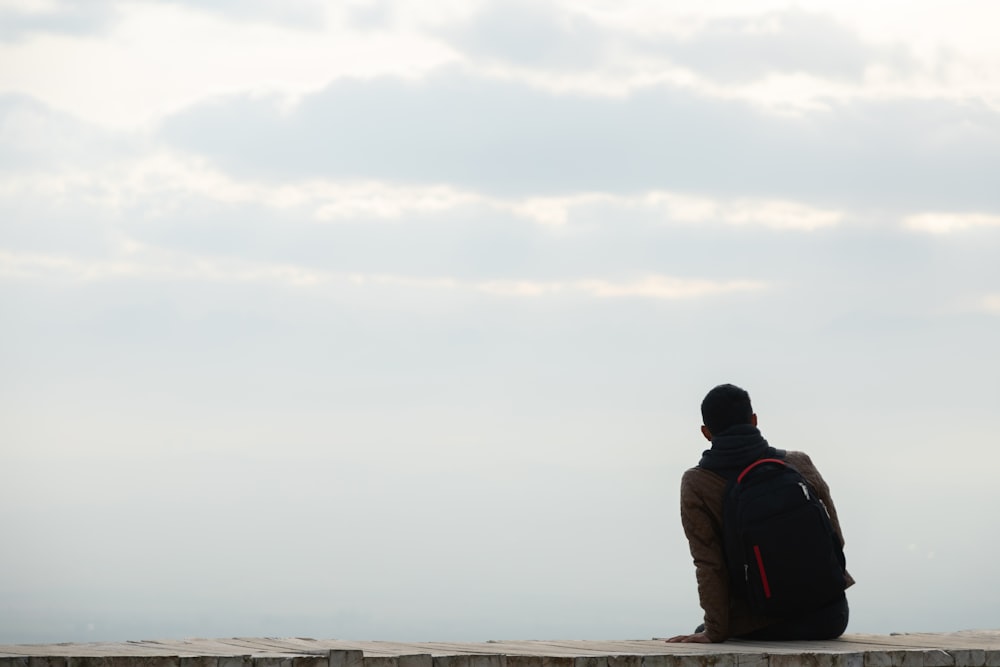 a person sitting on a ledge with a backpack