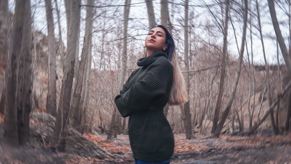 a woman standing in the woods with her arms crossed