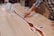 A person is working on a wooden table with artistic inlays, using a tool to shape or fill a resin river design. The surface is predominantly light-colored wood, and there are various white outlines possibly marking where resin will be placed.