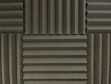 Various panels with a grooved pattern arranged in a symmetrical manner. The panels have a textured surface and appear to be made of foam material, commonly used for soundproofing.