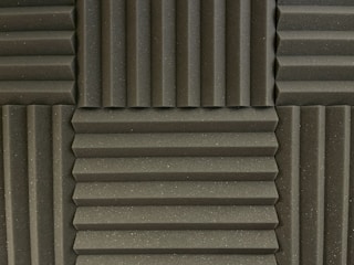 Various panels with a grooved pattern arranged in a symmetrical manner. The panels have a textured surface and appear to be made of foam material, commonly used for soundproofing.