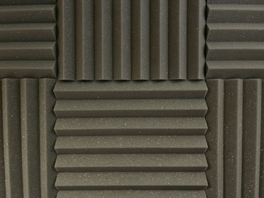 Various panels with a grooved pattern arranged in a symmetrical manner. The panels have a textured surface and appear to be made of foam material, commonly used for soundproofing.