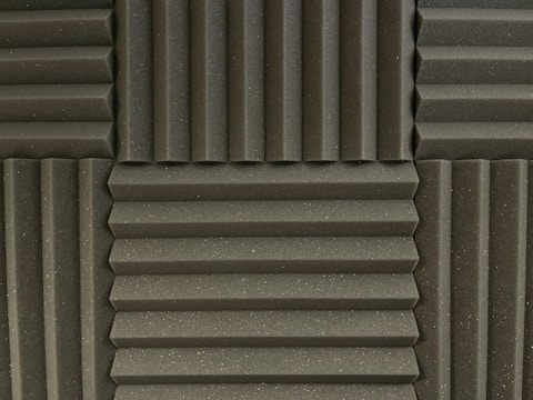 Various panels with a grooved pattern arranged in a symmetrical manner. The panels have a textured surface and appear to be made of foam material, commonly used for soundproofing.