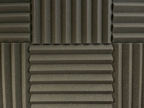 Various panels with a grooved pattern arranged in a symmetrical manner. The panels have a textured surface and appear to be made of foam material, commonly used for soundproofing.