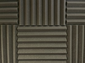 Various panels with a grooved pattern arranged in a symmetrical manner. The panels have a textured surface and appear to be made of foam material, commonly used for soundproofing.
