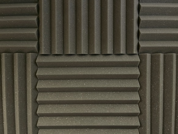 Various panels with a grooved pattern arranged in a symmetrical manner. The panels have a textured surface and appear to be made of foam material, commonly used for soundproofing.