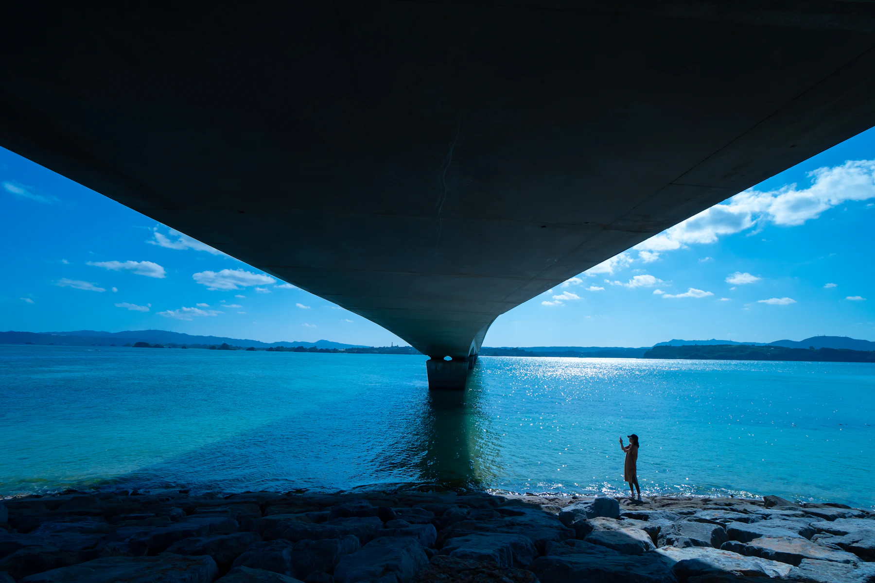 Blick unter einer langen Meeresbrücke auf blaues Wasser und Inselküste in Okinawa