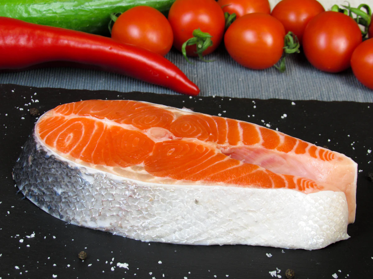 Filé de salmão cru sobre tábua com vegetais, exemplo de alimento com vitamina D dietética