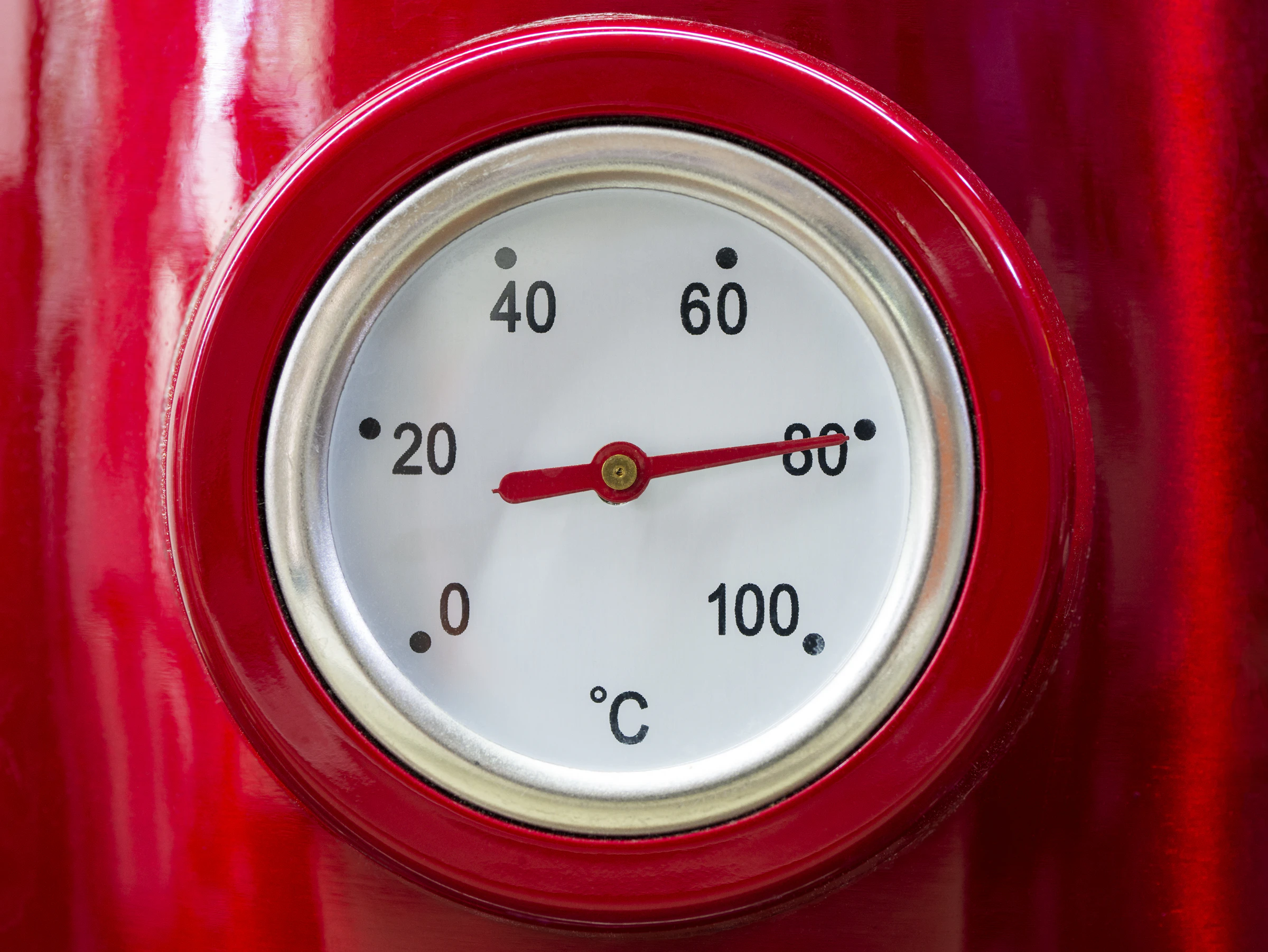 Close-up of a vintage red temperature gauge with the needle climbing past 80 degrees