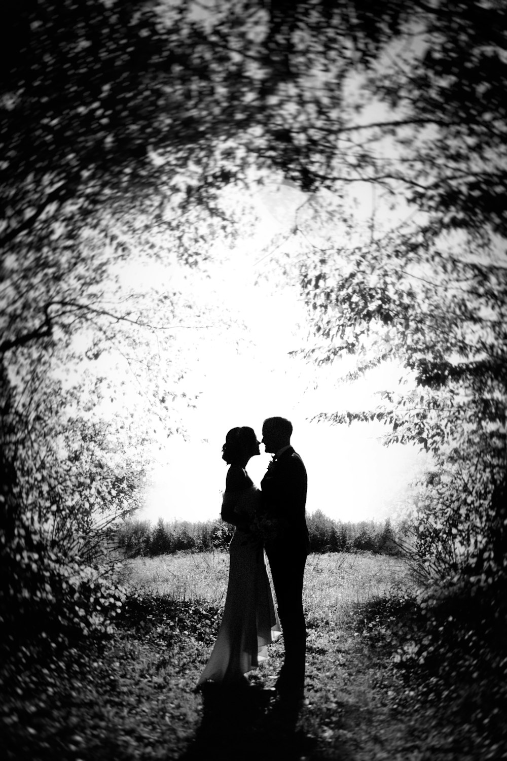 a black and white photo of a couple standing in the woods