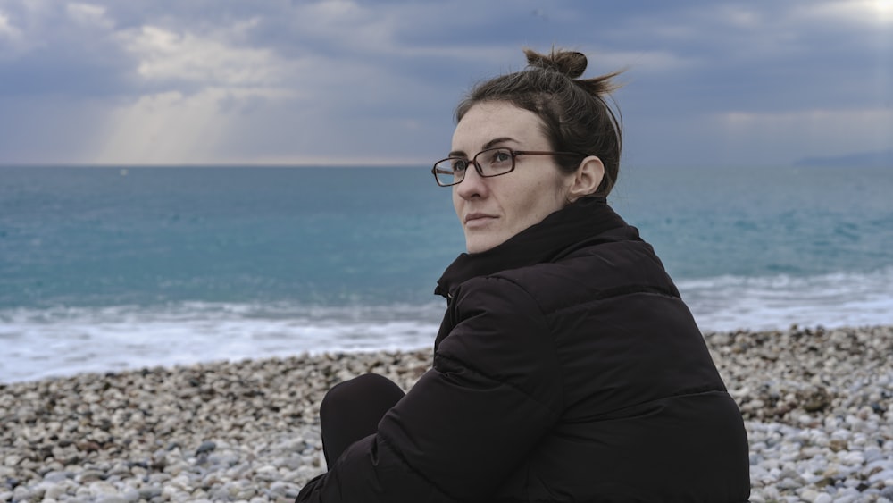 a woman sitting on a beach next to the ocean