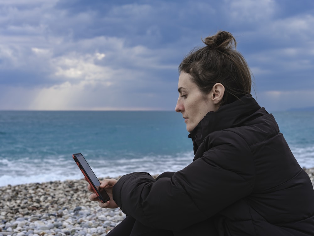 a woman sitting on the beach looking at her cell phone