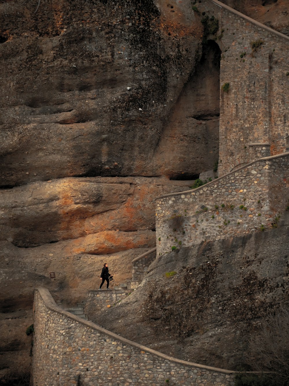 a person walking up a stone wall next to a cliff