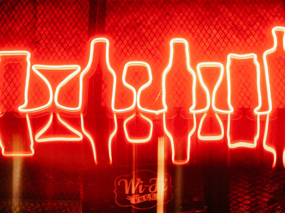 a neon display of bottles and glasses in front of a red wall