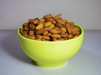 Close-up of glossy almonds spilling from a rustic wooden bowl on a light green background