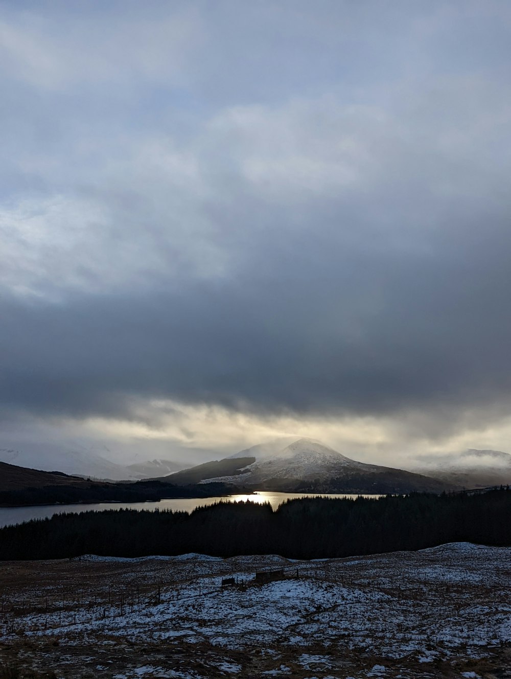 a cloudy sky over a lake with mountains in the background