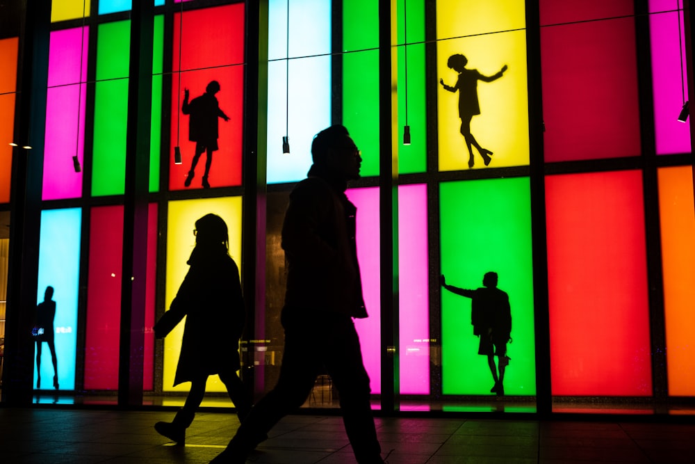 silhouettes of people walking in front of a multicolored building