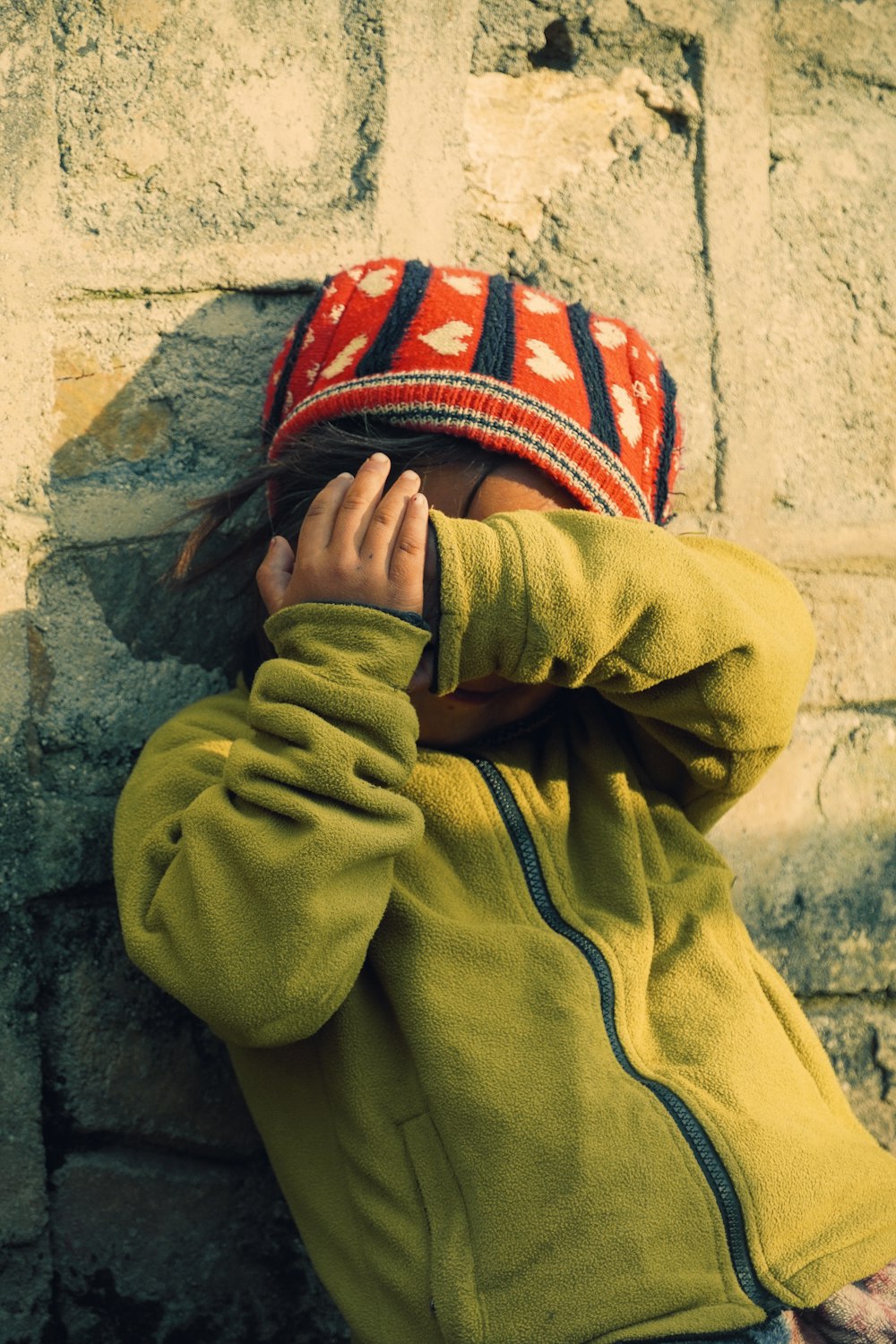 a young child is leaning against a brick wall