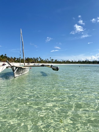 A traditional boat gently floating near a white sandy beach under a bright blue sky.