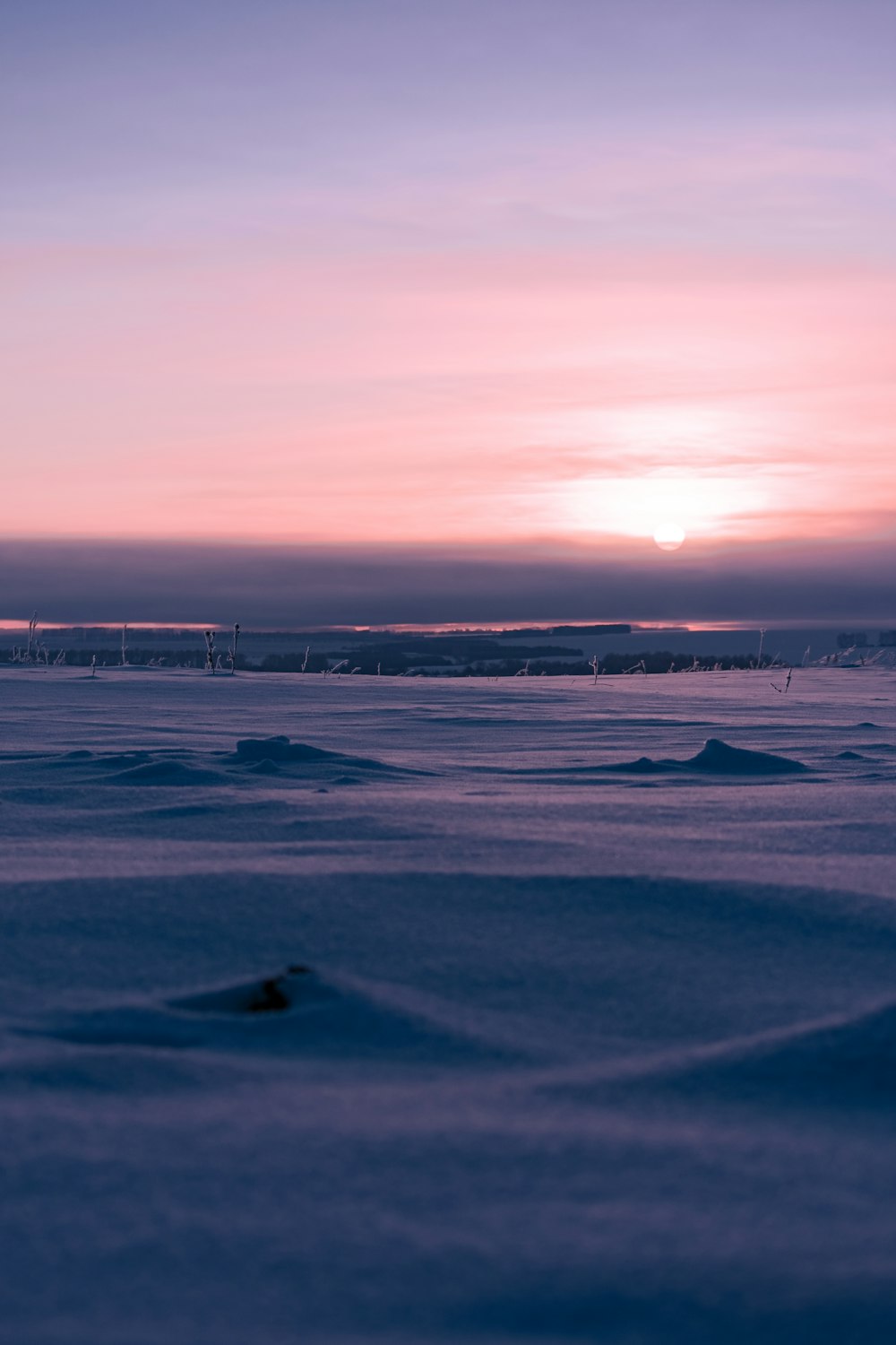 the sun is setting over a snowy field