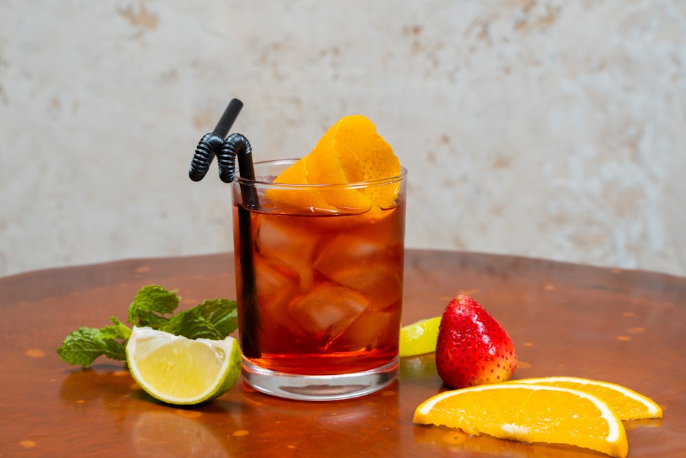 a glass of iced tea with a straw, lemon, and strawberries