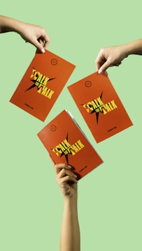 Three hands hold orange booklets with the title 'Walk the Talk' in bold, yellow letters. The backgrounds are a solid light green color.