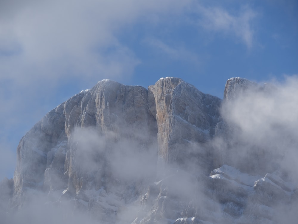 a mountain covered in snow and clouds under a blue sky