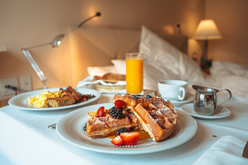 a breakfast of waffles, fruit, and coffee on a bed