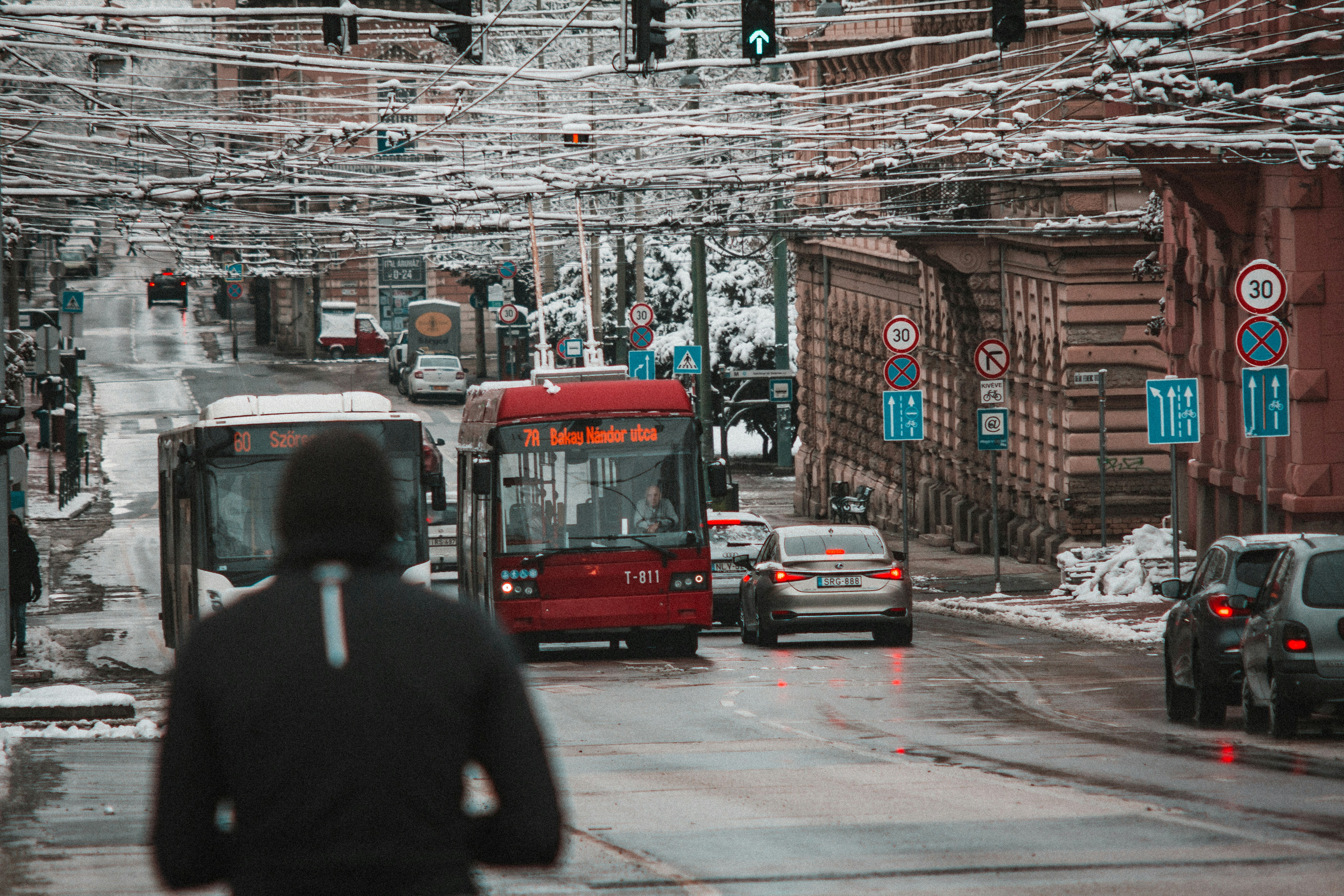 a man walking across a street next to a red bus