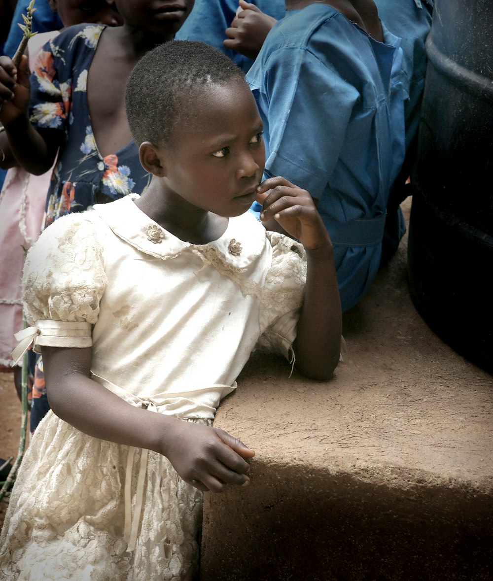 a young girl in a white dress standing in front of a group of children