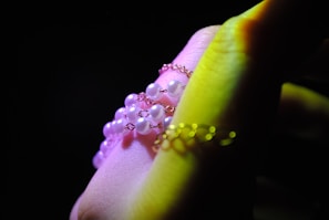 A close-up of a hand adorned with delicate jewelry, featuring pearl-like beads strung together with fine metal chains. The hand is partially illuminated, creating a soft glow on the skin and jewelry.