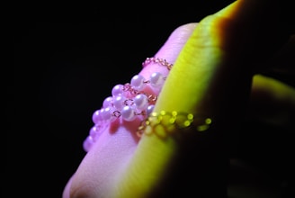 A close-up of a hand adorned with delicate jewelry, featuring pearl-like beads strung together with fine metal chains. The hand is partially illuminated, creating a soft glow on the skin and jewelry.