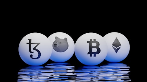 Four spherical objects are placed on a reflective surface with a black background. Each sphere has a cryptocurrency symbol: Tezos, Dogecoin, Bitcoin, and Ethereum. The spheres emit a blue glow, reflecting off the surface below.
