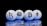 Four spherical objects are placed on a reflective surface with a black background. Each sphere has a cryptocurrency symbol: Tezos, Dogecoin, Bitcoin, and Ethereum. The spheres emit a blue glow, reflecting off the surface below.