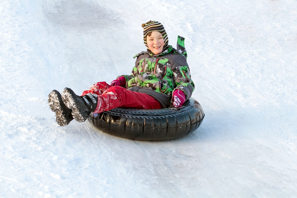 雪に覆われた斜面をスノーチューブに乗って下る少年