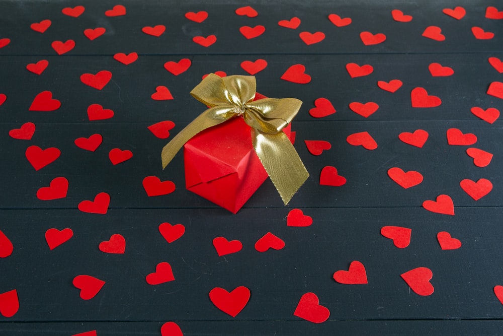 eine rote Geschenkbox mit goldener Schleife auf schwarzem Grund mit roten Herzen