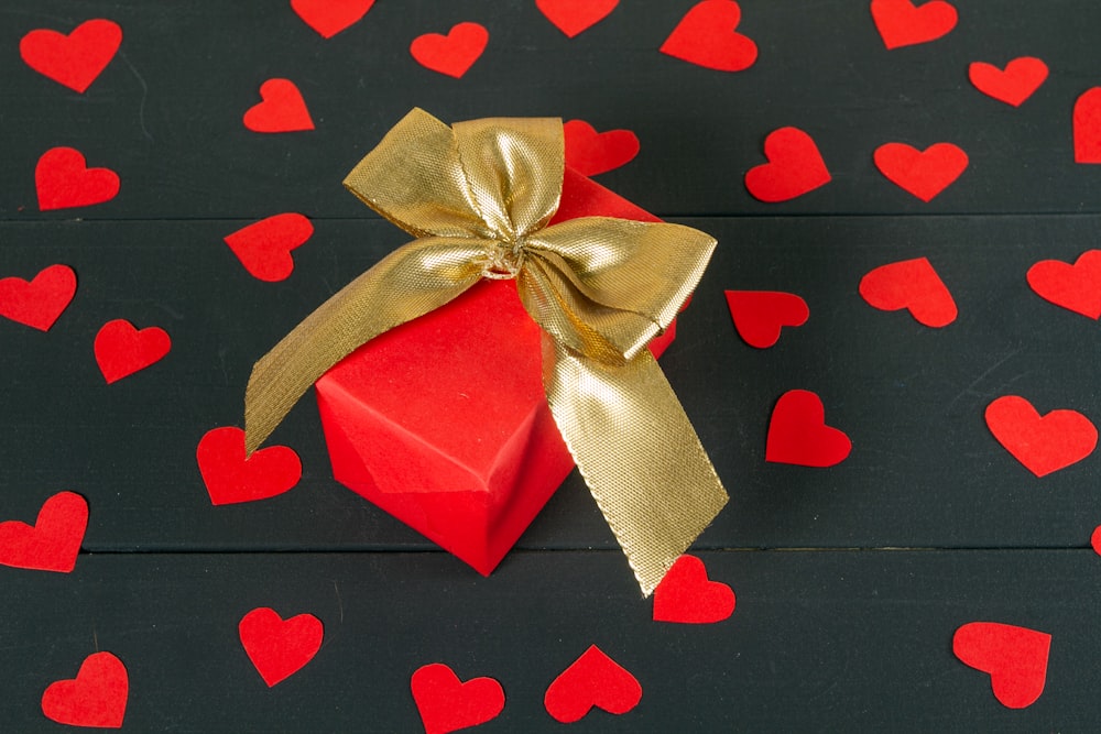 Un coffret cadeau rouge avec un nœud doré sur fond noir avec des cœurs rouges