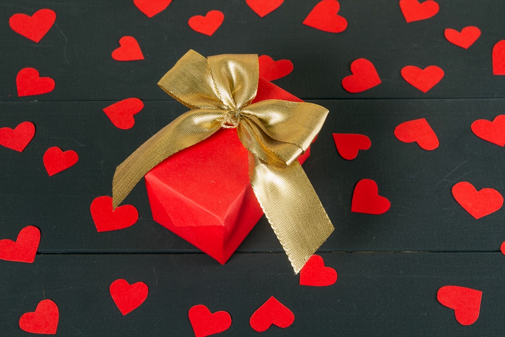 a red gift box with a gold bow on a black background with red hearts