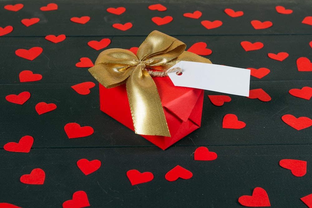 a red gift box with a gold bow and a white card