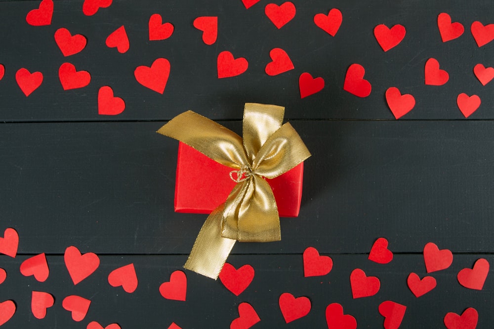 a red gift box with a gold ribbon and a bow