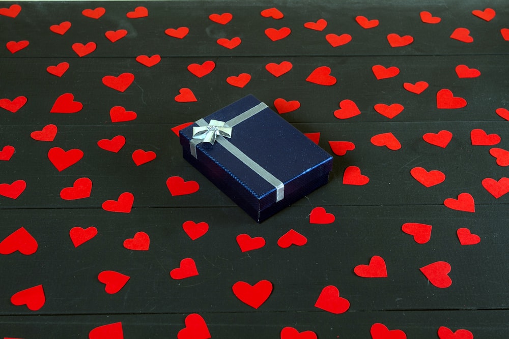 eine blaue Geschenkbox auf einem mit Herzen bedeckten Tisch