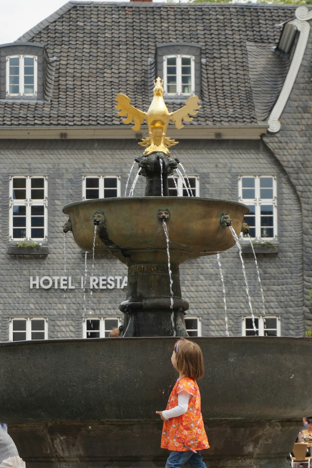a little girl that is standing in front of a fountain