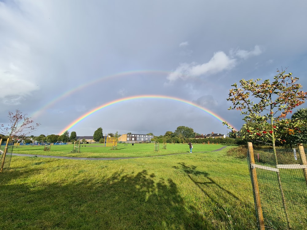 a rainbow appears over a grassy field with a house in the background