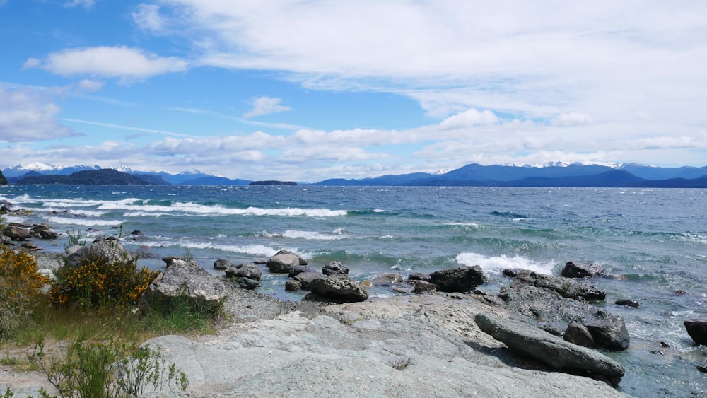 a rocky shore with a body of water and mountains in the background