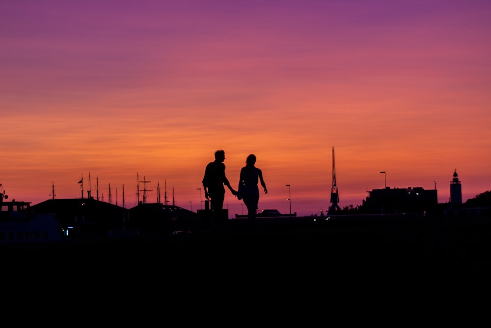 a couple of people walking across a field at sunset
